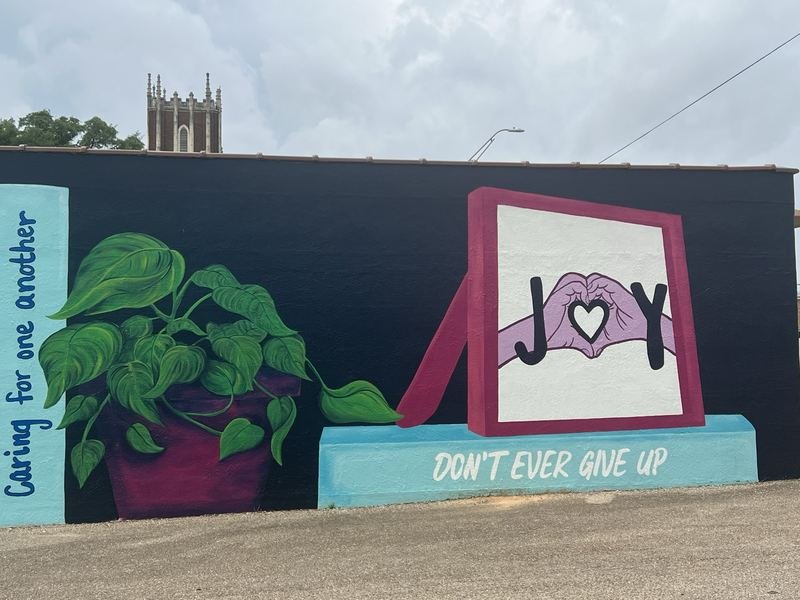 The JOY bookshelf mural in downtown Waco — giant painted book spines with hopeful titles, ending in a framed JOY where two hands form a heart