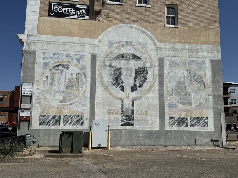 The faded Heart to Heart mural on the rear wall of the Praetorian Building in Waco: Christ with arms outstretched before a cross, between medallions of the U.S. Capitol and a Russian Orthodox cathedral, above the inscription NOT ONLY FOR US in English and Russian